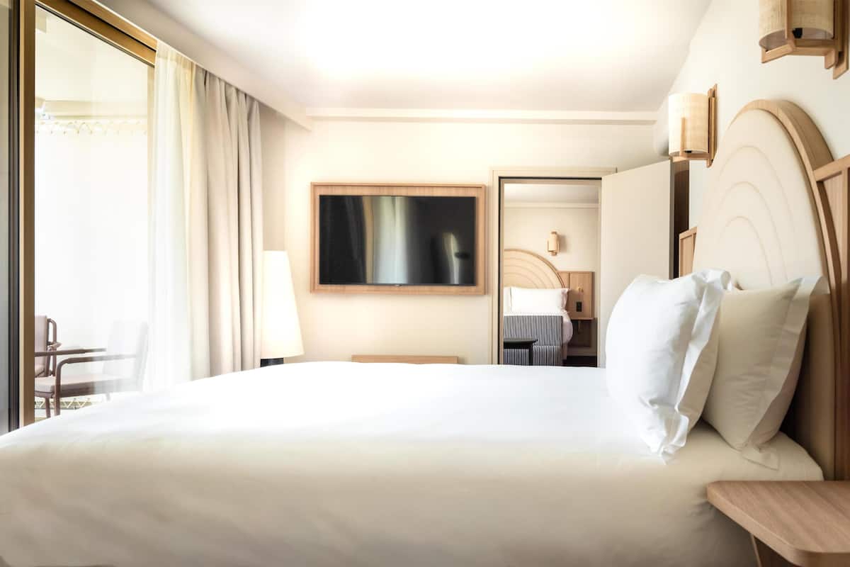 Habitación de hotel con una cama grande, un escritorio, una silla, un televisor y un baño visible a través de una puerta abierta.