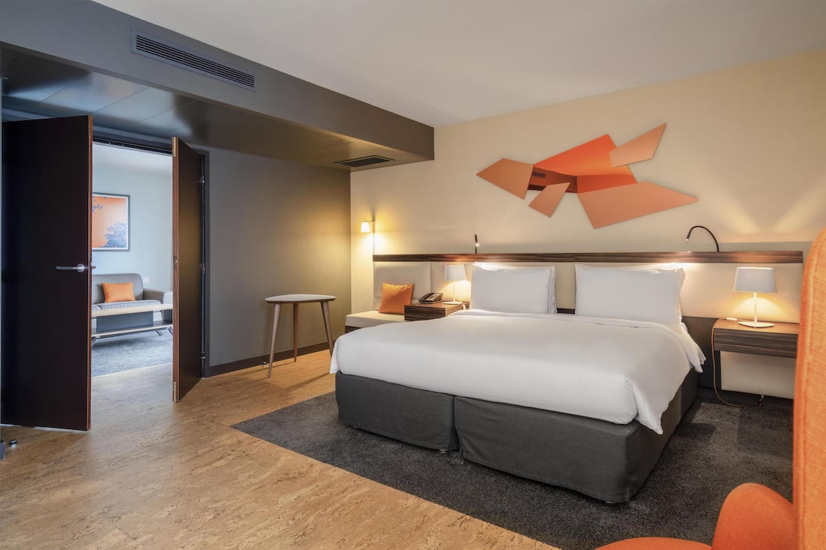 Une chambre d’hôtel moderne avec un grand lit, des tables de chevet, une œuvre d’art murale et une vue sur la chambre voisine.