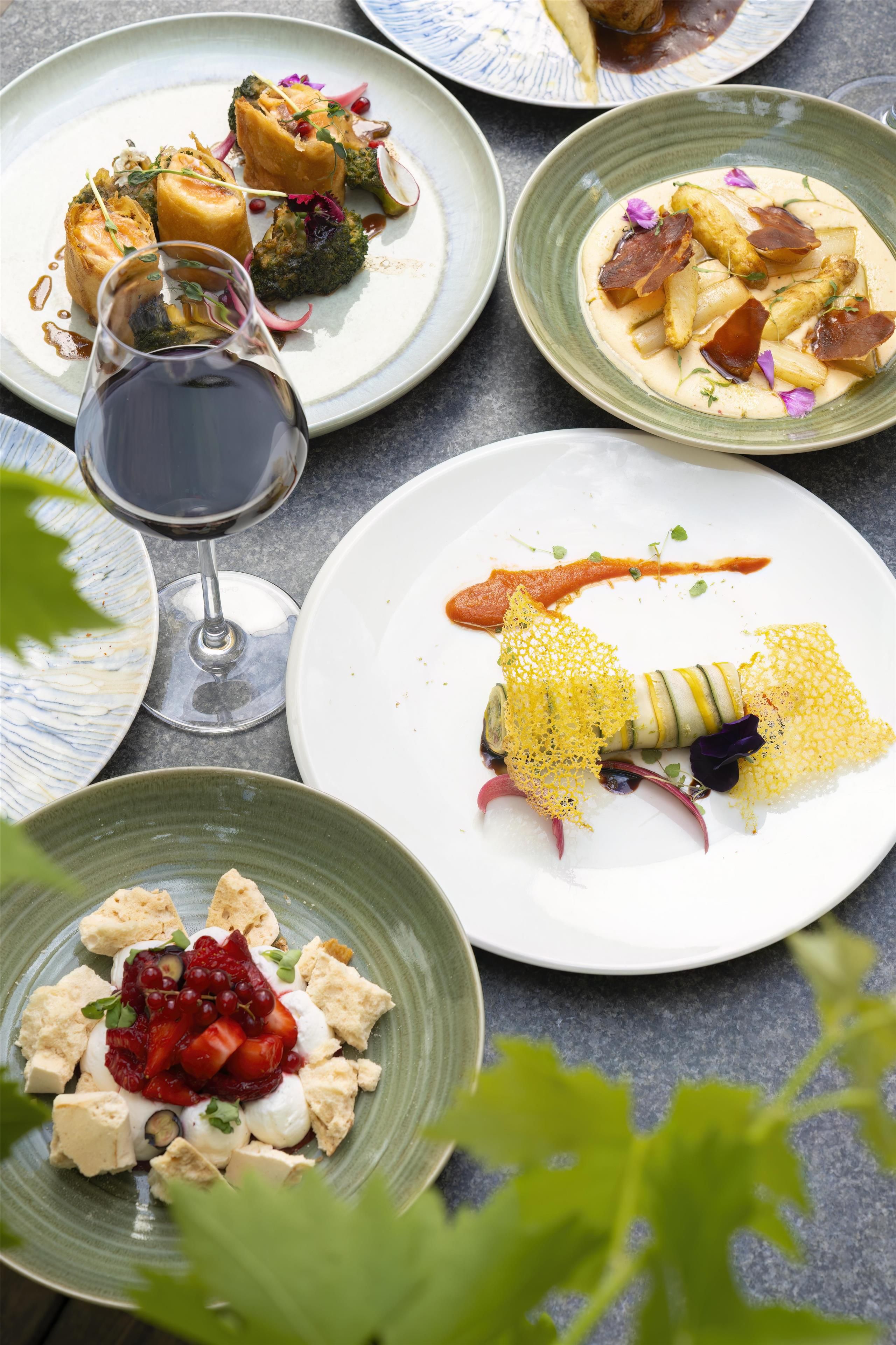 A variety of dishes on plates, a glass of red wine, and a table setting.