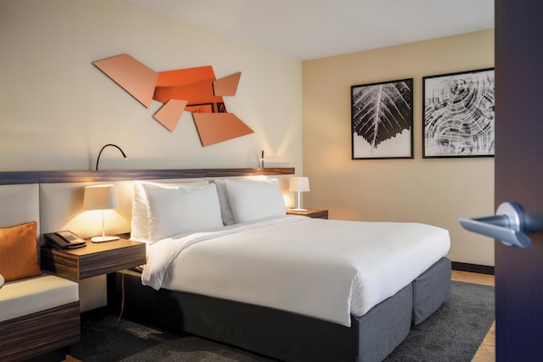 Habitación de hotel con cama, mesitas de noche, lámpara y cuadros en la pared.