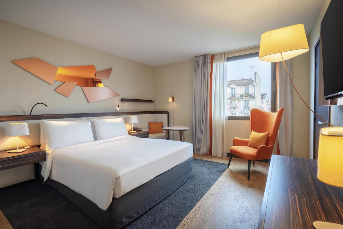 Une chambre d’hôtel avec un grand lit, un bureau, une chaise, une télévision et une fenêtre avec des rideaux.