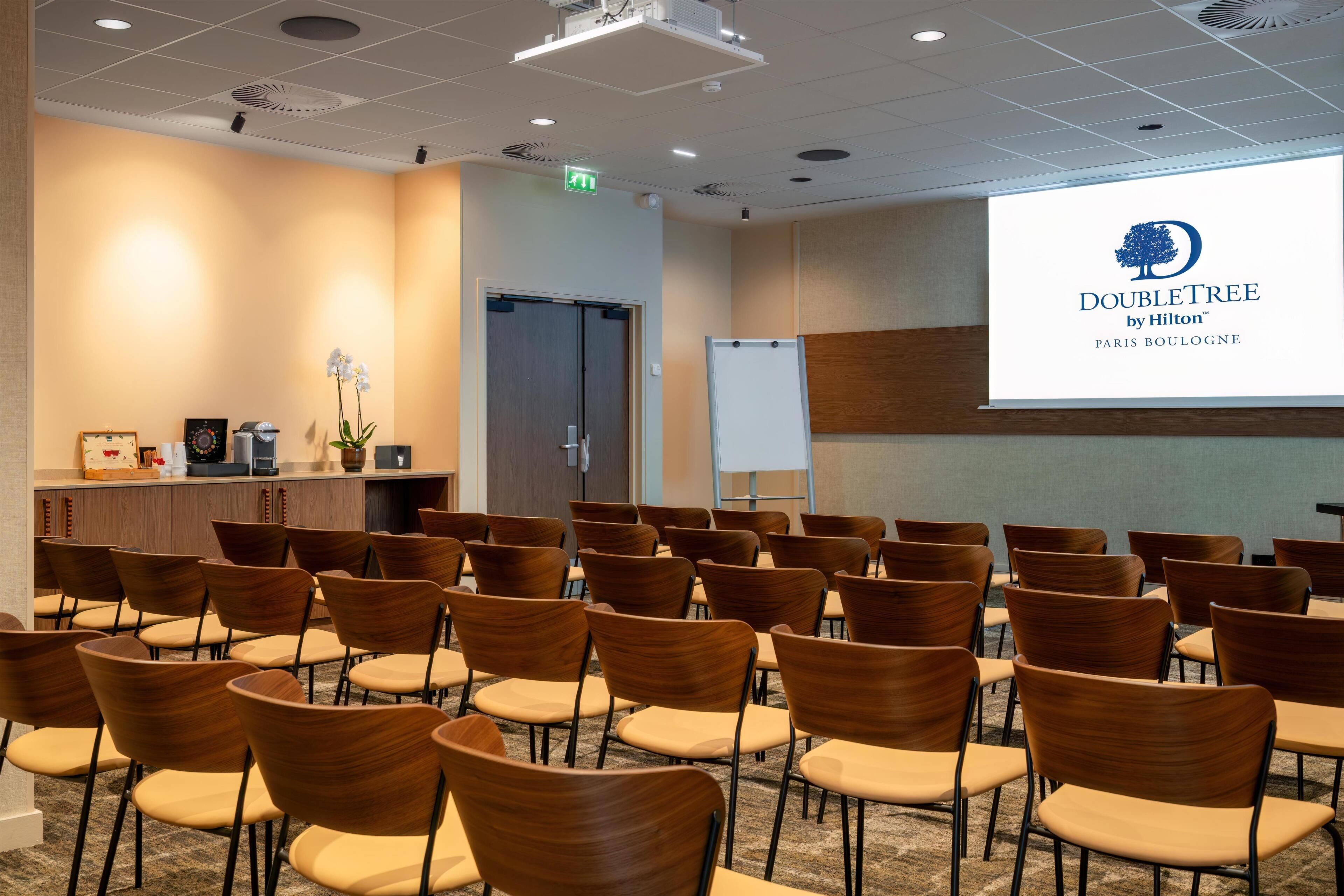 A conference room with rows of wooden chairs, a podium, and a projection screen displaying the DoubleTree by Hilton logo.