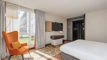 Una habitación de hotel con una cama, una silla, un televisor y vistas al exterior.