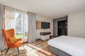 A hotel room with a bed, a chair, a television, and a view of the outside. - Doubletree By Hilton Paris Boulogne (Boulogne-Billancourt)