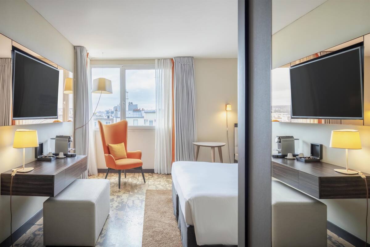 Une chambre d’hôtel avec deux lits, un bureau, une chaise, une petite table, une télévision et une fenêtre avec des rideaux.