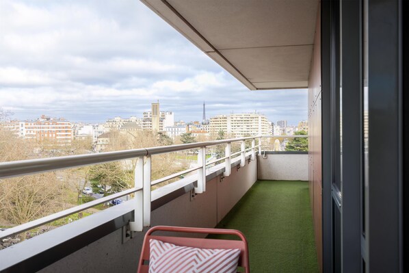 A balcony with a view of a cityscape, a metal chair, and a small patch of artificial grass. - Doubletree By Hilton Paris Boulogne (Boulogne-Billancourt)