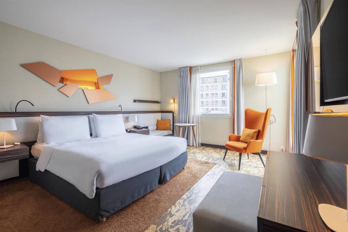 Une chambre d’hôtel avec un lit, un bureau, une chaise, une télévision et une fenêtre avec des rideaux.