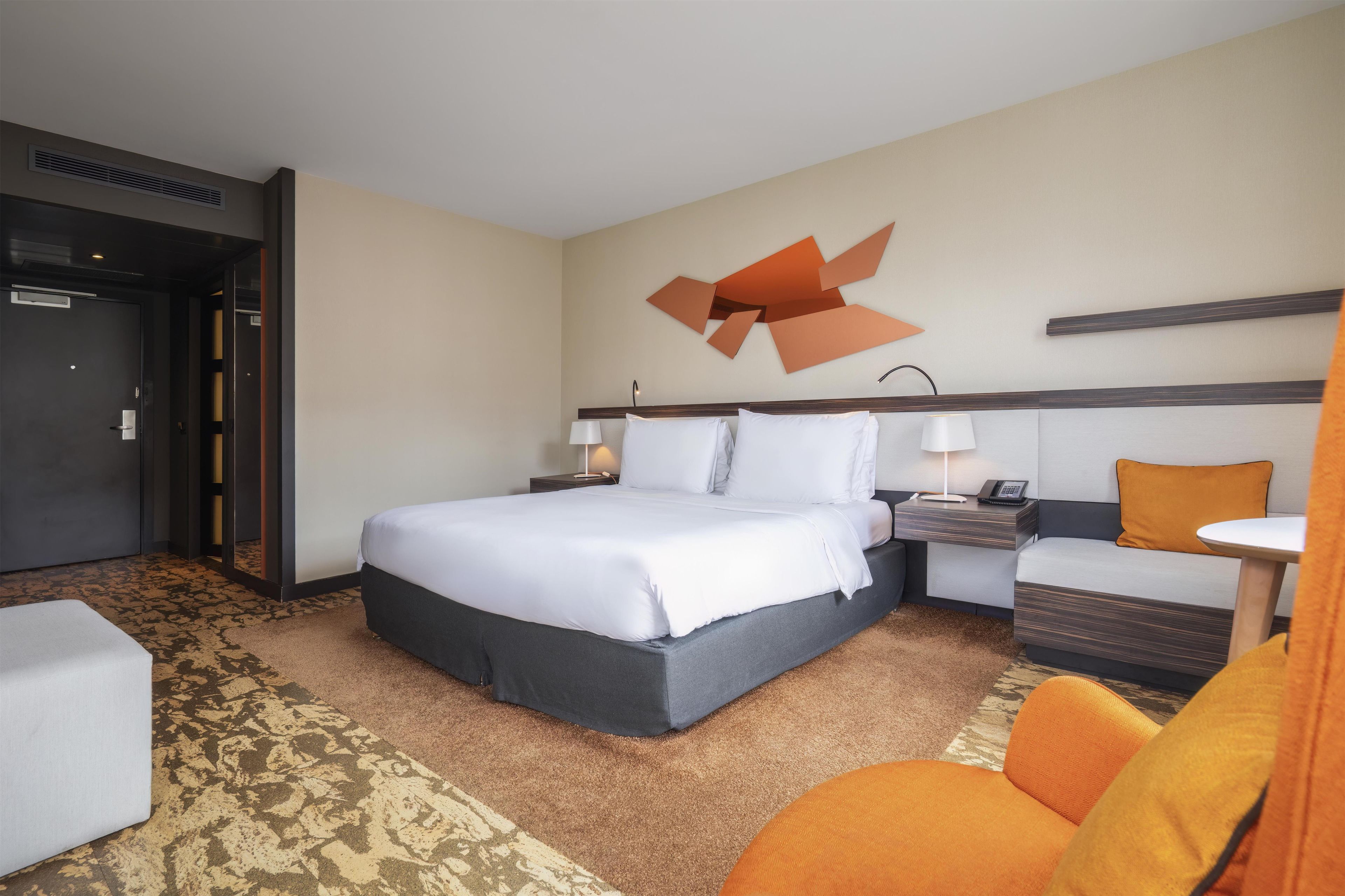 Una habitación de hotel con cama, mesitas de noche, escritorio, silla y alfombra estampada.