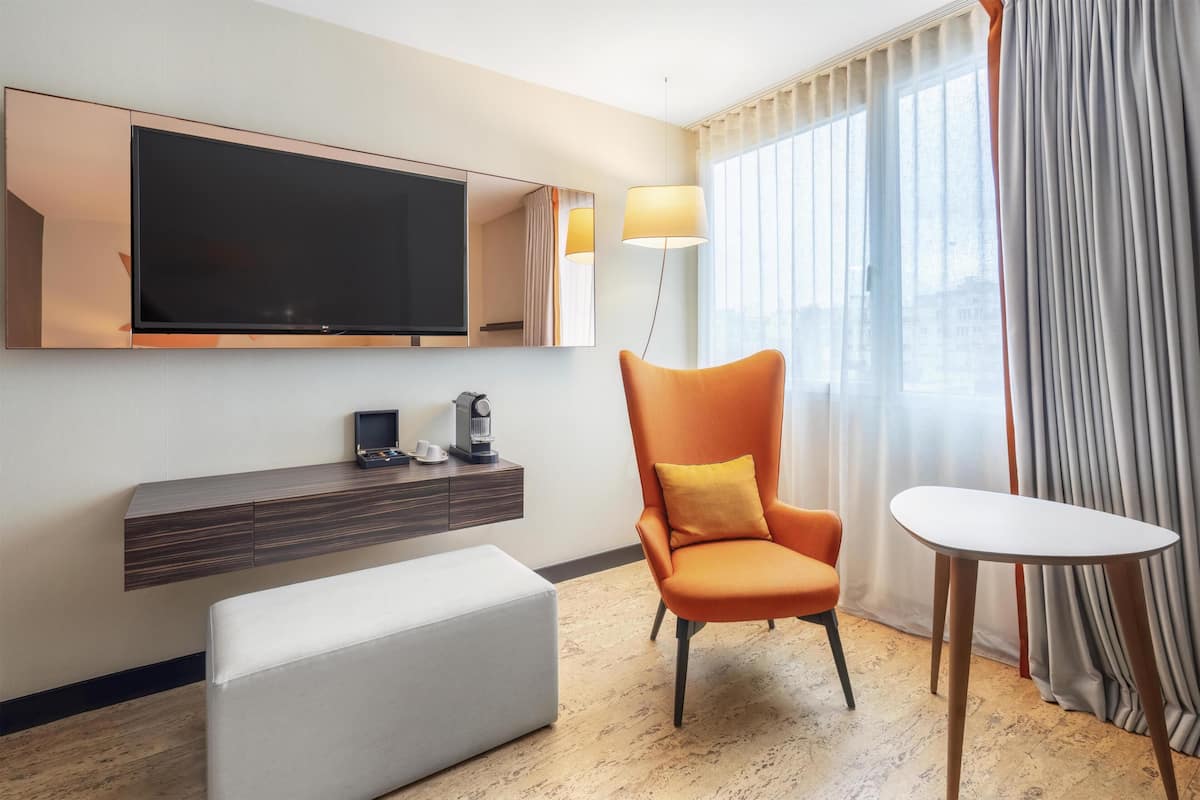 Une chambre d’hôtel équipée d’un téléviseur à écran plat, d’un canapé, d’un fauteuil, d’une petite table et d’une lampe.