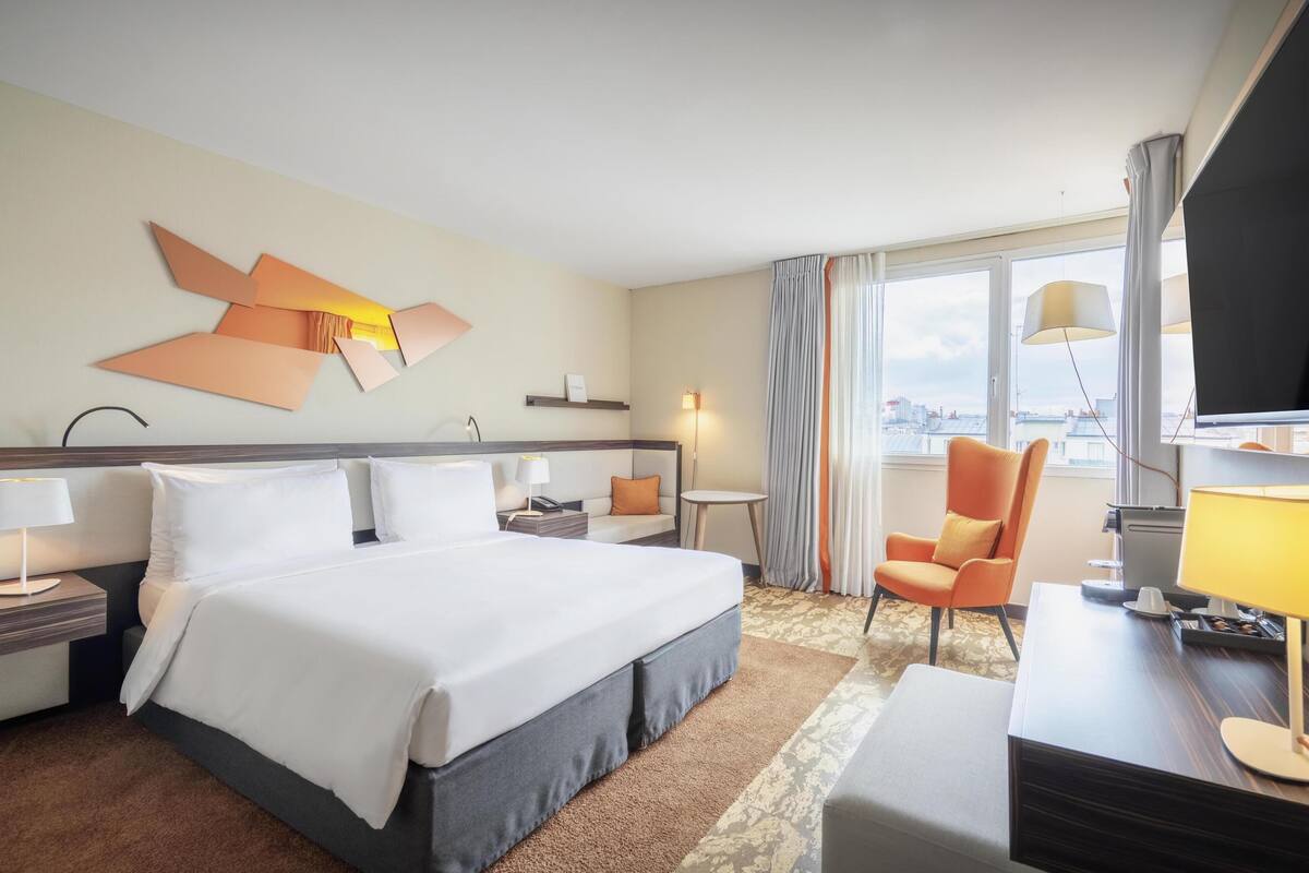 Une chambre d’hôtel avec un grand lit, un bureau, une chaise, une télévision et une vue sur la ville.
