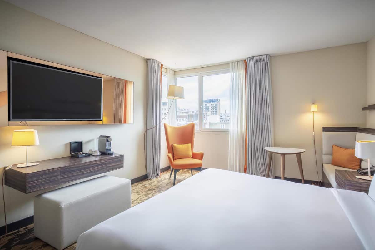 Une chambre d’hôtel comprenant un lit, un bureau avec un téléviseur à écran plat, une chaise, une petite table et une lampe.