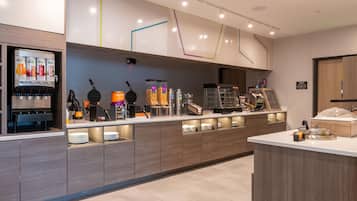 Un bar à petit-déjeuner moderne équipé d’une machine à gaufres, d’une machine à café et d’un distributeur de jus.