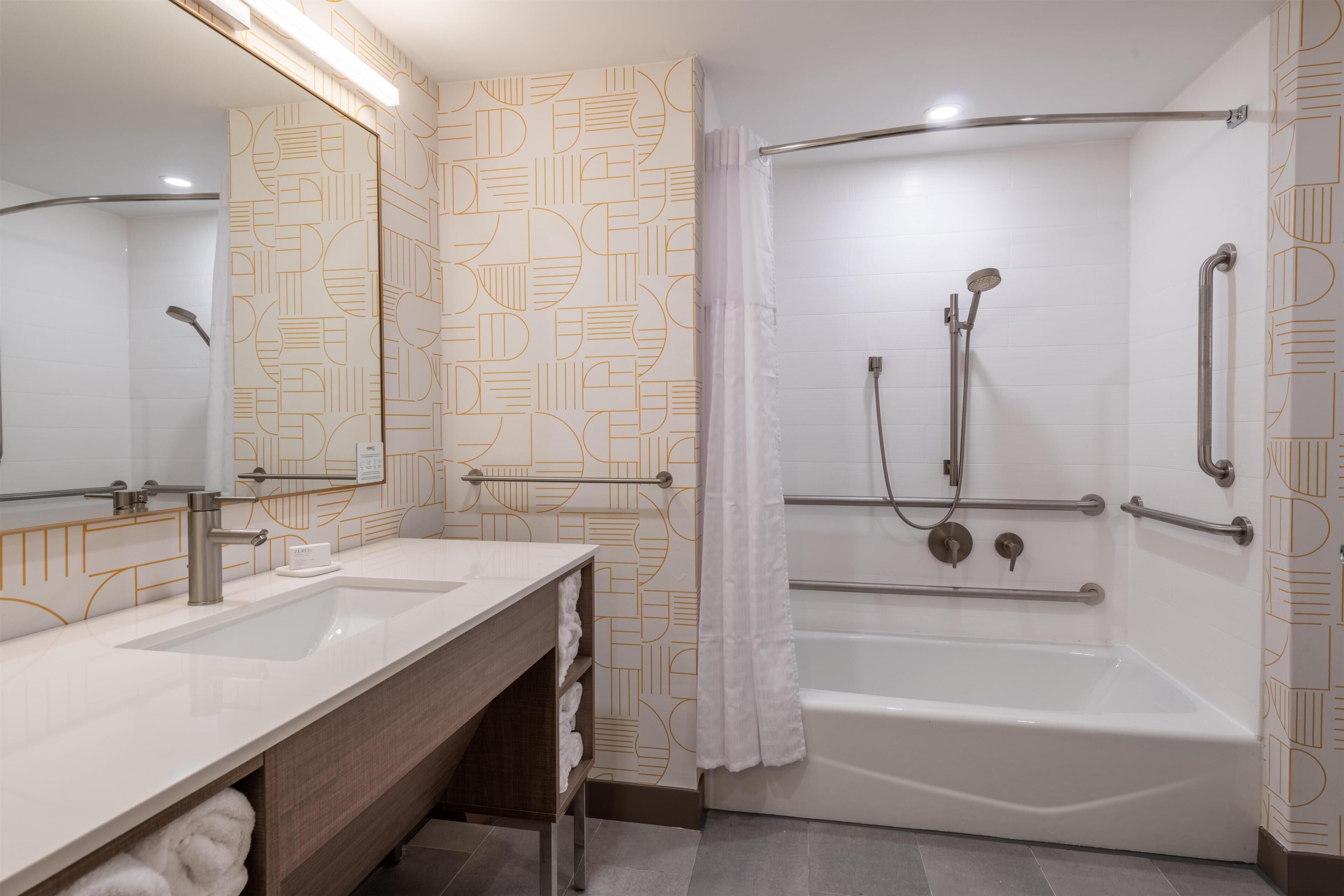 A modern bathroom with a double sink vanity, a walk-in shower with grab bars, and a large mirror.