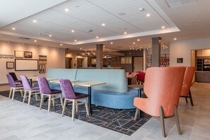Un hall de hotel con una zona de estar que incluye sillas moradas, un sofá azul y una silla roja con estampado.