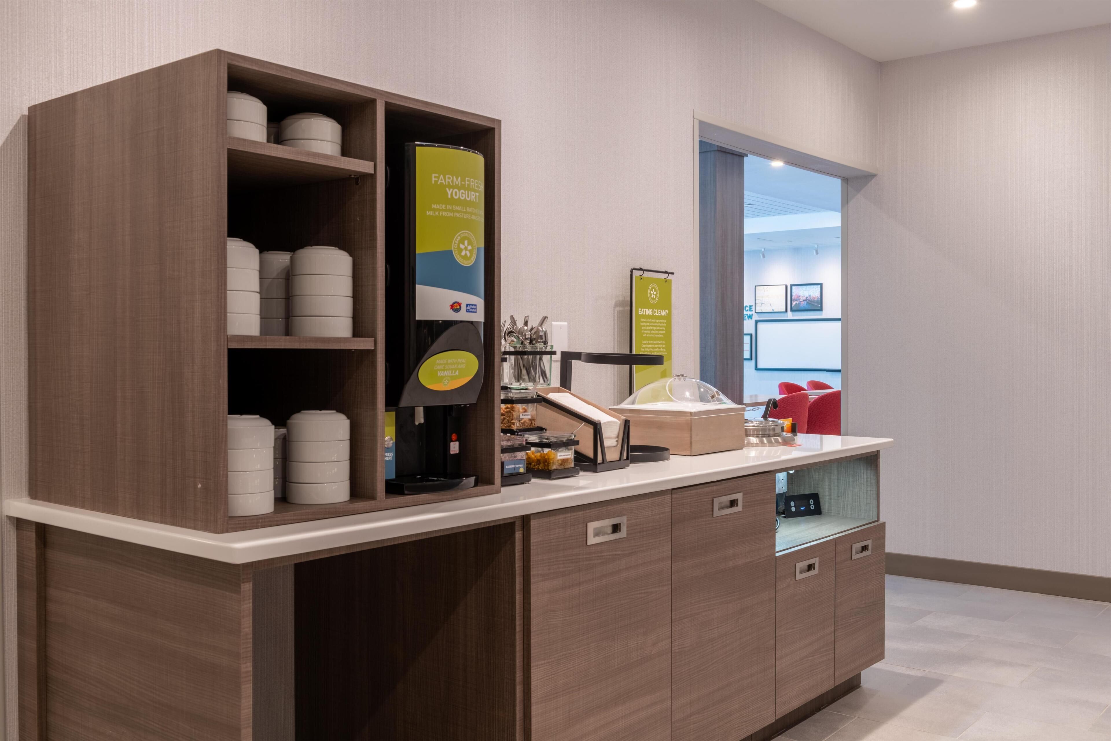 Een moderne kitchenette met een koffieapparaat, een yoghurtdispenser en een glazen vitrine.