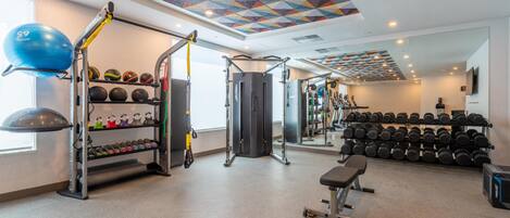 Ein Fitnessraum mit unterschiedlicher Trainingsausstattung, darunter ein Squat-Gestell, Medizinbälle und Kurzhanteln.