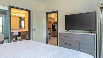 Habitación de hotel con cama, televisor, armario y baño visible a través de una puerta abierta.