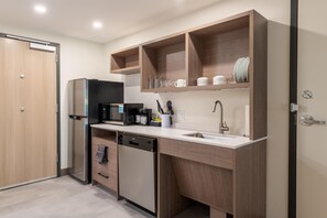 Una cocina compacta con refrigerador, microondas, cafetera y lavamanos.