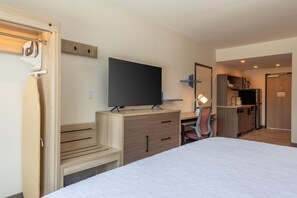 Habitación de hotel con cama, escritorio con televisor de pantalla plana, silla, espejo y kitchenette.