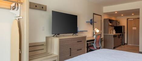 Une chambre d’hôtel comprenant un lit, un bureau avec un téléviseur à écran plat, une chaise, un miroir et une kitchenette.