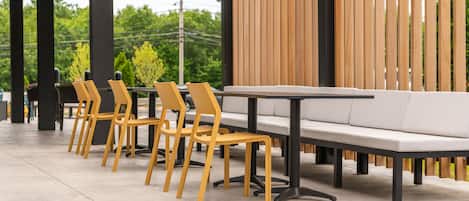 A modern outdoor seating area with a row of yellow chairs and a white sofa, a concrete floor, and a wooden slatted wall in the background.