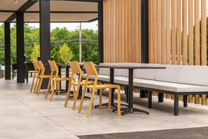 Un espace extérieur moderne, aménagé avec des sièges, comprenant une rangée de chaises jaunes et un canapé blanc, un sol en béton et un mur en bois à lattes en arrière-plan.