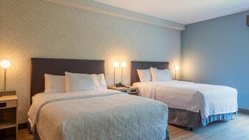 Habitación de hotel con dos camas, cada una con cabecera, mesitas de noche y lámparas.