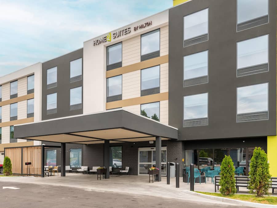 A modern hotel with a covered entrance, outdoor seating, and a clear sky.