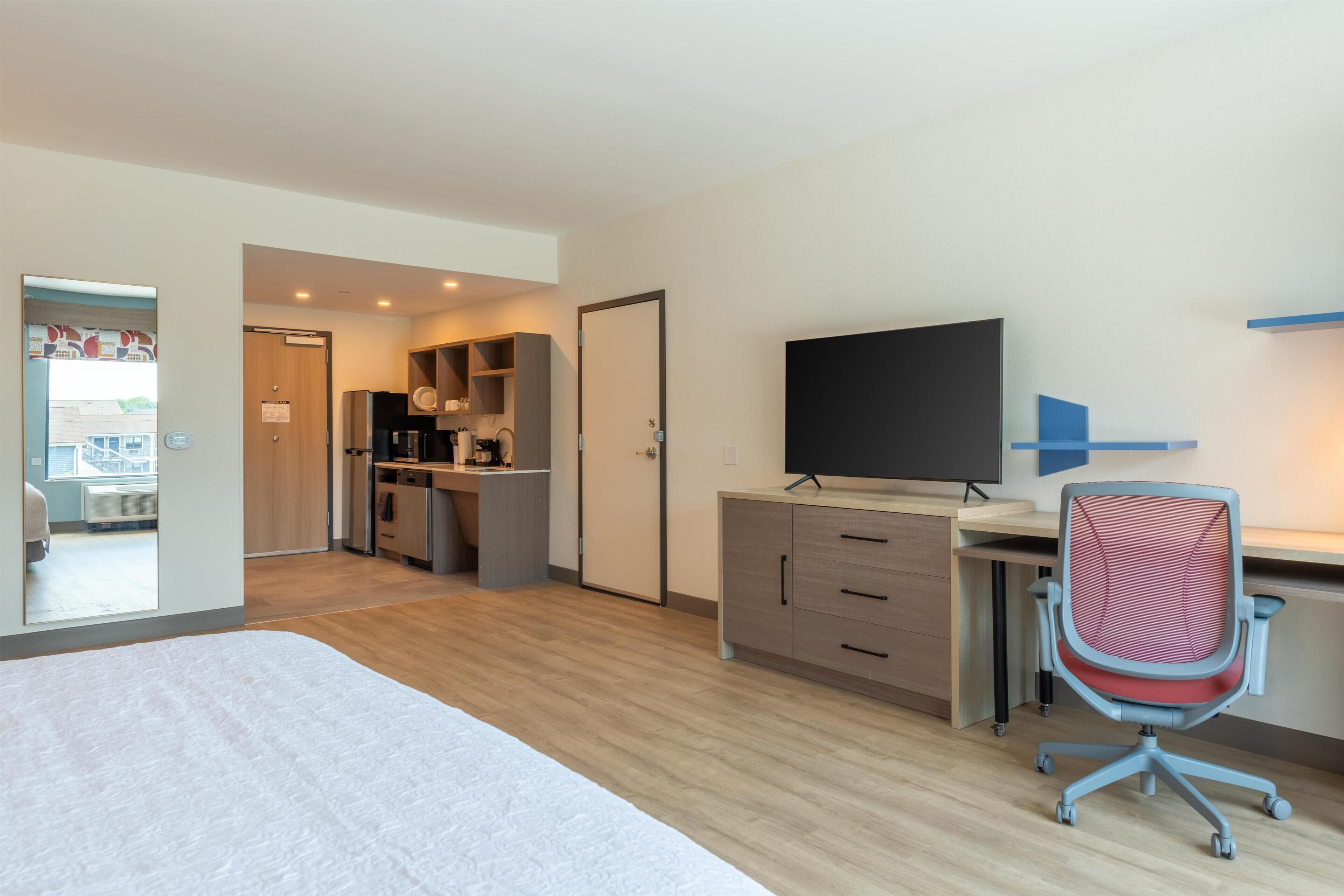 Quarto de hotel com uma cama, uma escrivaninha com computador, televisão e uma kitchenette.