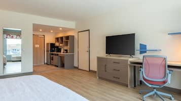 Quarto de hotel com uma cama, uma escrivaninha com computador, televisão e uma kitchenette.