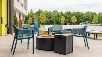 An outdoor patio area with green metal chairs and a round table with a fire pit.