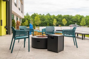 Un espacio al aire libre con sillas metálicas verdes y una mesa redonda con una chimenea.