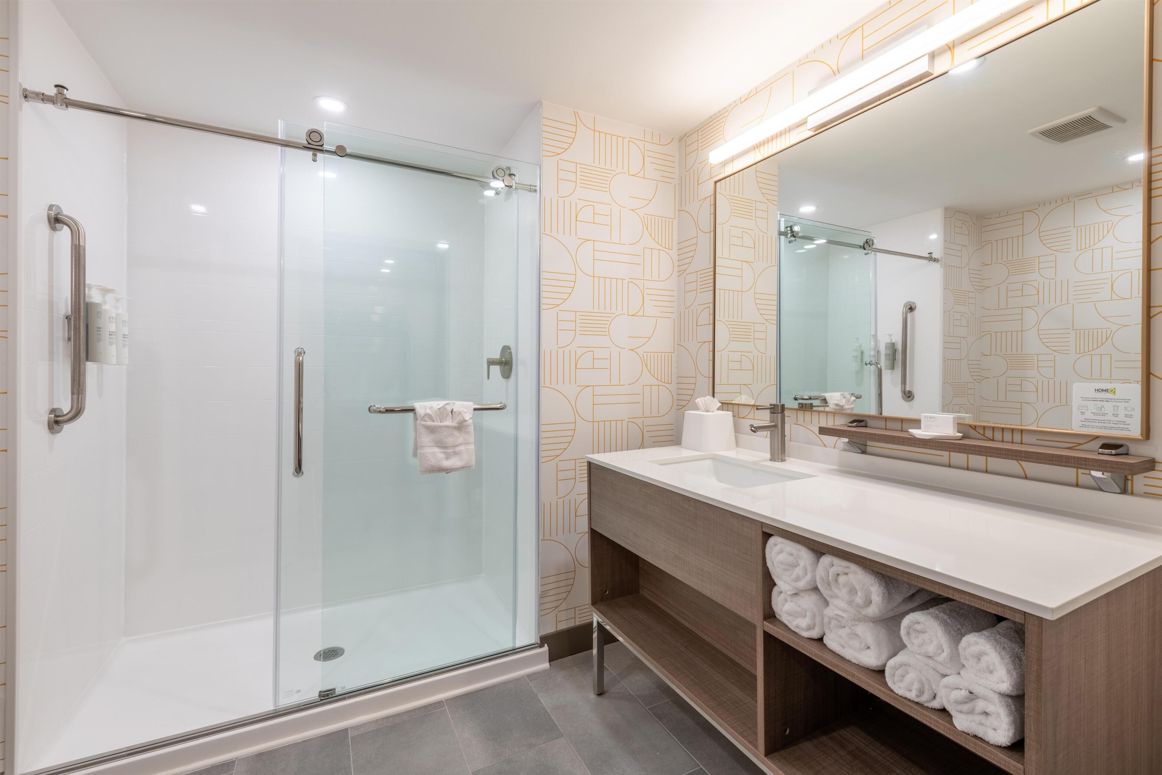 Une salle de bain moderne avec une douche à parois de verre, un meuble-lavabo doté d’un grand miroir et un porte-serviettes.