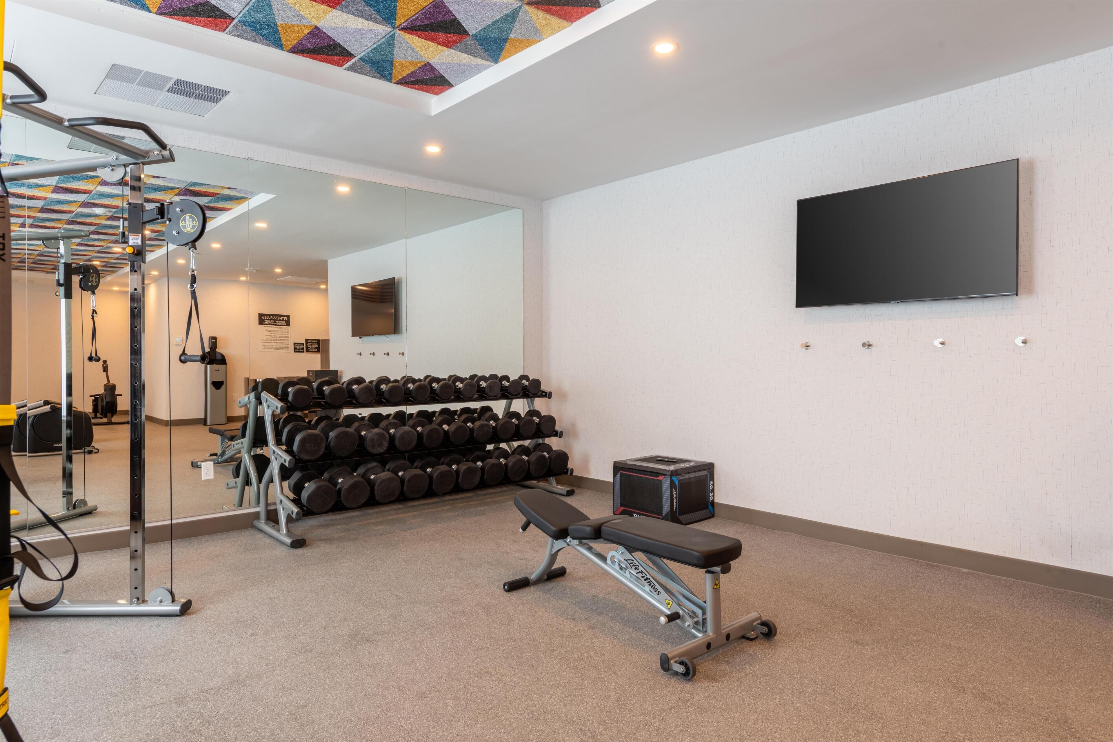 Un gimnasio con equipo de ejercicio, una banca y un televisor montado en la pared.