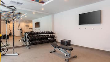 Un gimnasio con equipo de ejercicio, una banca y un televisor montado en la pared.