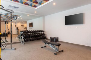 A gym with exercise equipment, a bench, and a TV mounted on the wall.