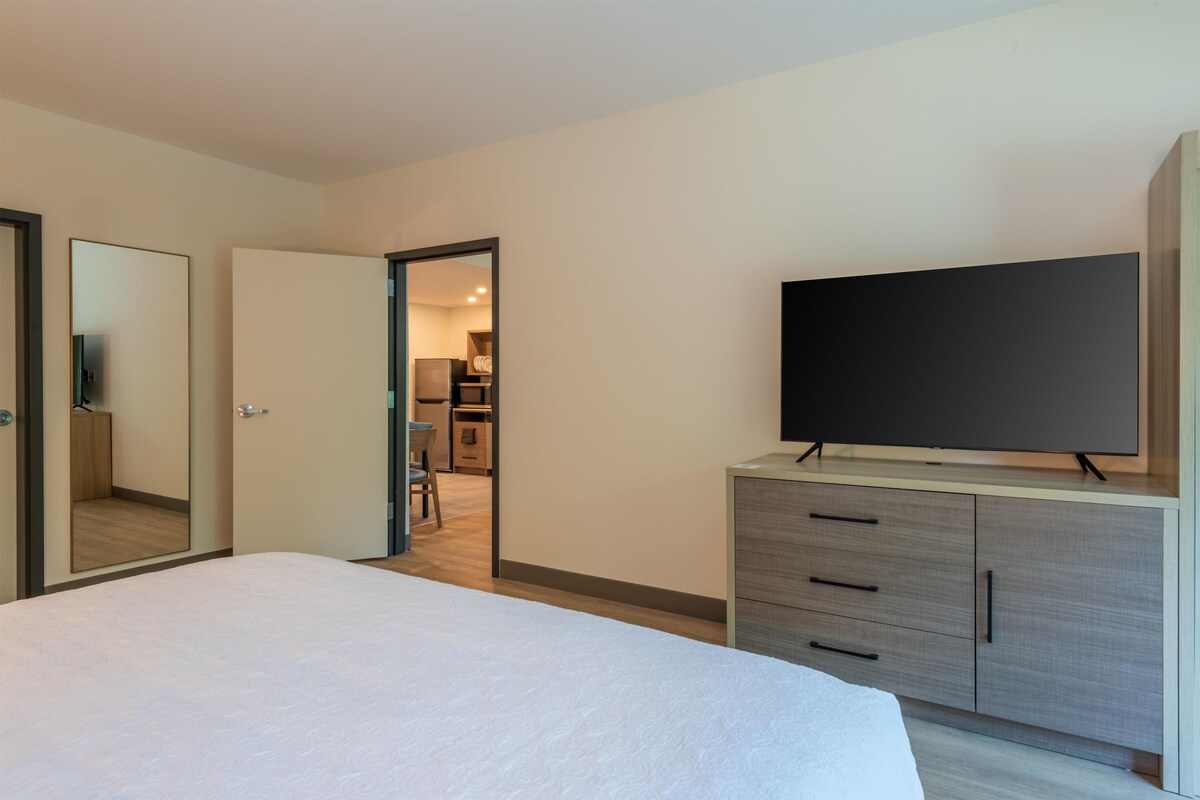 A hotel room with a bed, a TV on a stand, a wardrobe, and a mirror.