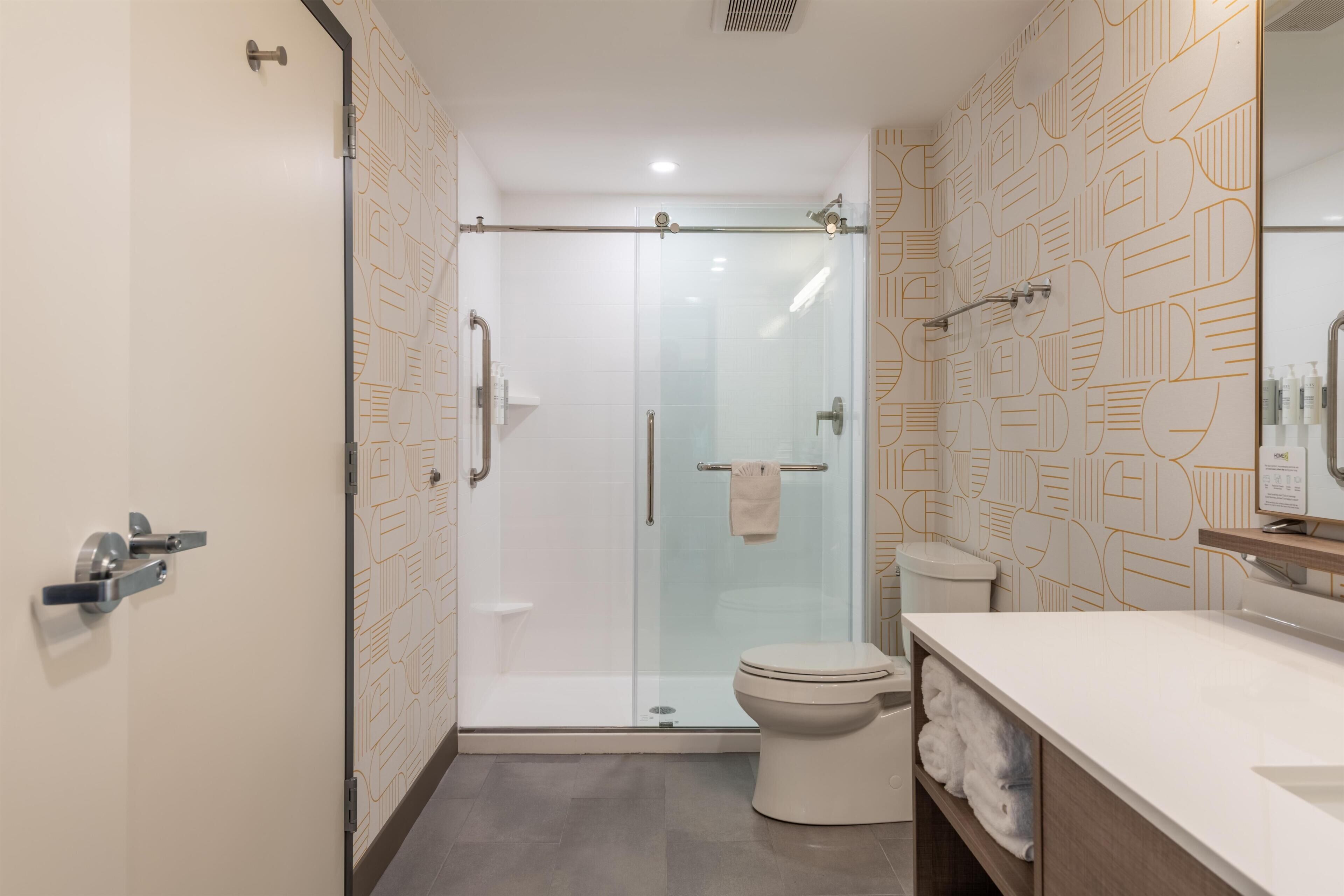 Un baño moderno con cabina de ducha de vidrio, un inodoro y un tocador con toallero.