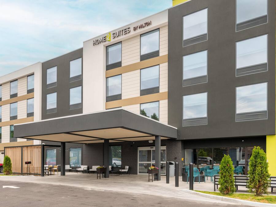 A modern hotel with a covered entrance, outdoor seating, and a clear sky.