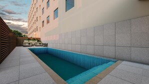 Ein moderner Außenpool mit Fliesenveranda, Holzzaun und Gebäude mit Kachelfassade.