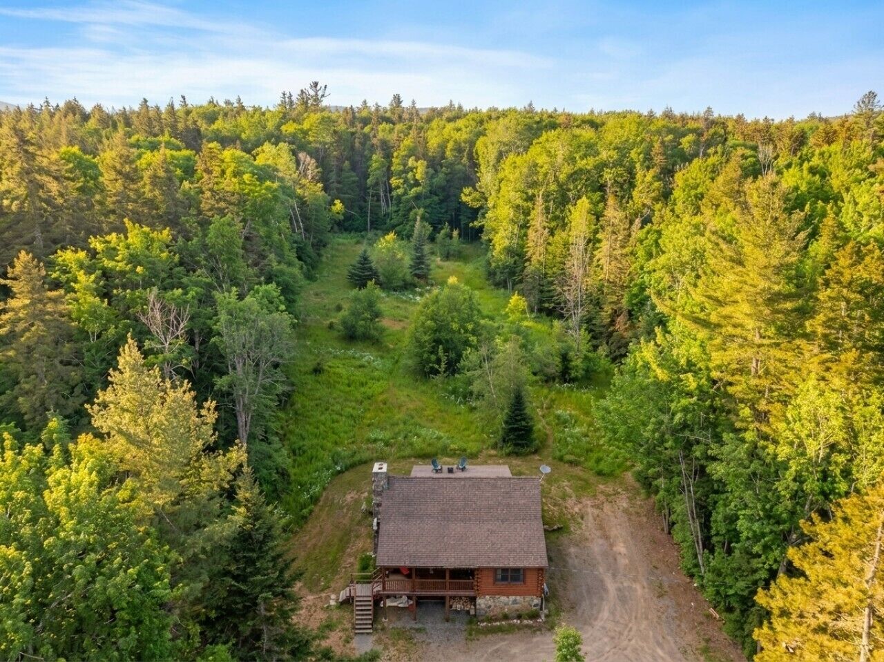 A cabin surrounded by dense forest, with a dirt path leading to the entrance.