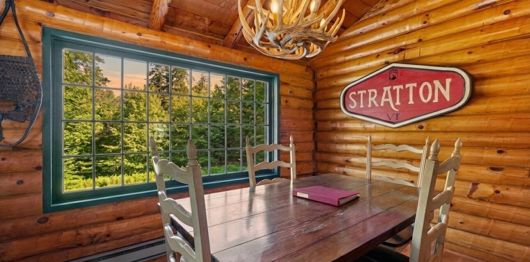 L’intérieur d’un chalet en bois, avec une table à manger, des chaises, une grande fenêtre et une enseigne sur laquelle on peut lire « STRATTON ».