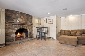A cozy living room with a stone fireplace, a wooden table with chairs, and a beige sofa.