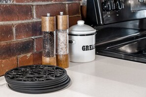A kitchen counter with a stack of black coasters, a white ceramic container labeled "GREASE," and two wooden salt and pepper shakers.
