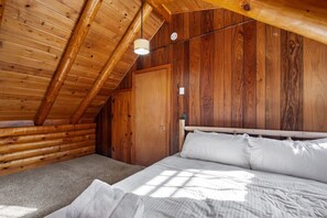 A wooden cabin bedroom with a sloped ceiling, a bed with white bedding, and a single light fixture.