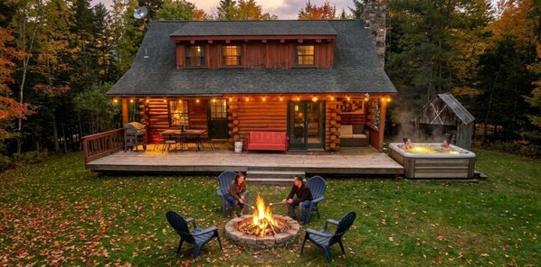 A log cabin with a deck, outdoor seating, a fire pit, and a hot tub.