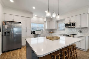A modern kitchen with white cabinets, stainless steel appliances, a large island with stools, and pendant lighting.