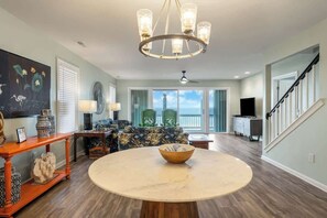A spacious living room with a round table, a chandelier, a sofa, and a television.