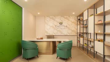 A wellness center with a reception desk, two green chairs, a marble wall with the logo 'TATTVA WELLNESS', and shelves with various items.