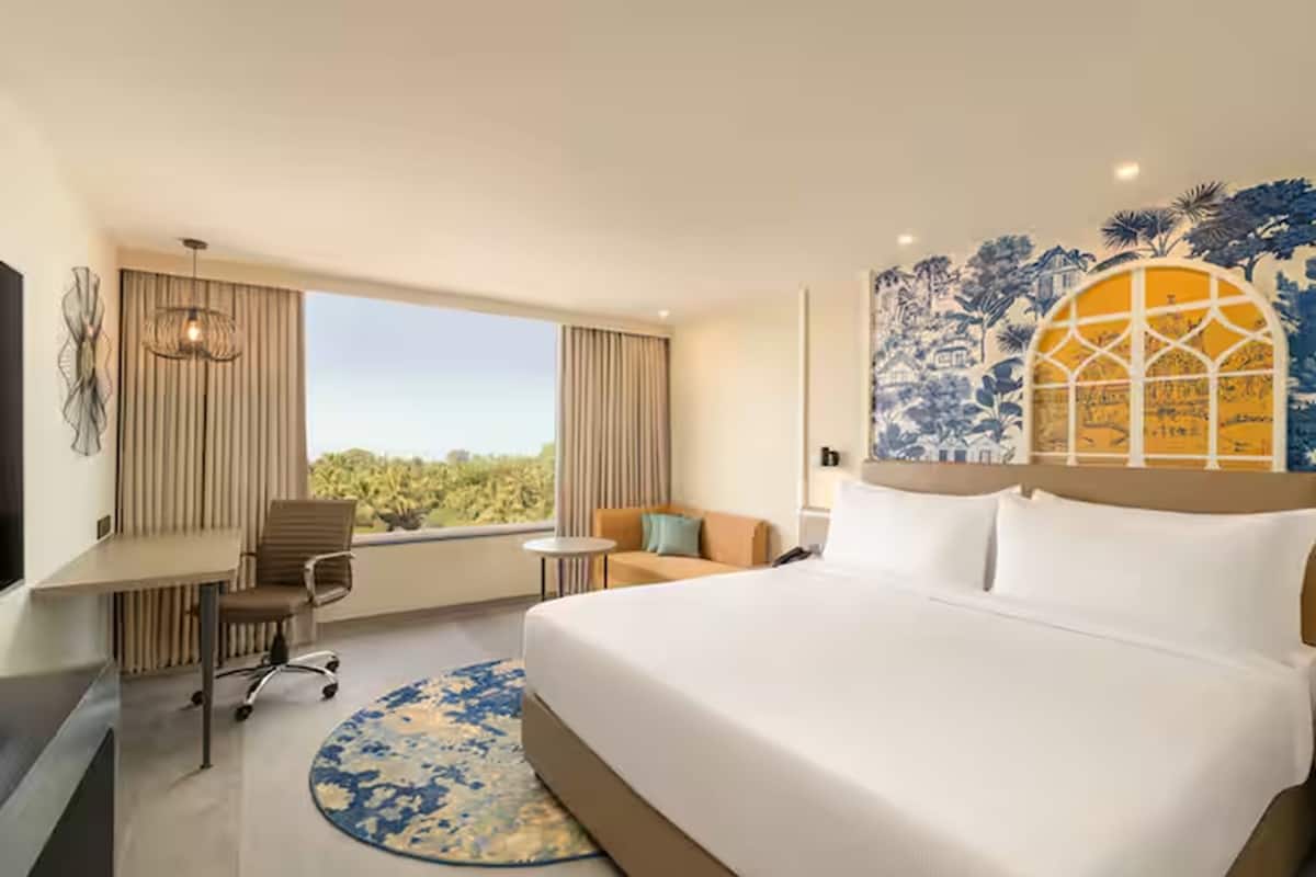 A hotel room with a large bed, a desk, a chair, a small round table, and a view of the outdoors.